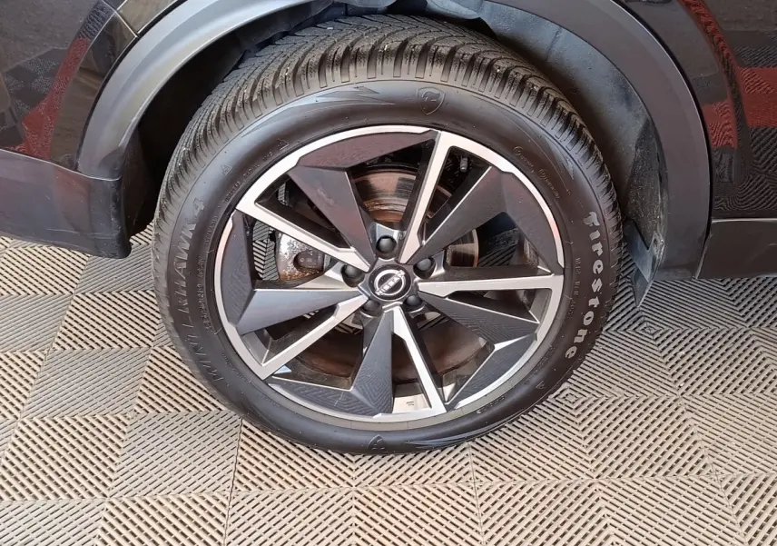 Gros plan sur la roue avant droite noire du Nissan Qashqai 2023 avec jante alliage bicolore et pneu Firestone.