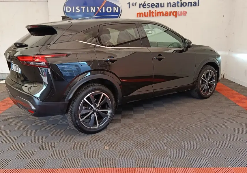 Vue 3/4 arrière droite du Nissan Qashqai noir 2023, avec jantes alliage et toit spoiler visible en intérieur showroom.