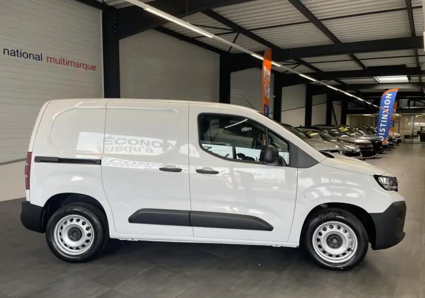 Vue de profil côté droit d'un Peugeot Partner blanc avec jantes tôles grises en intérieur de showroom.