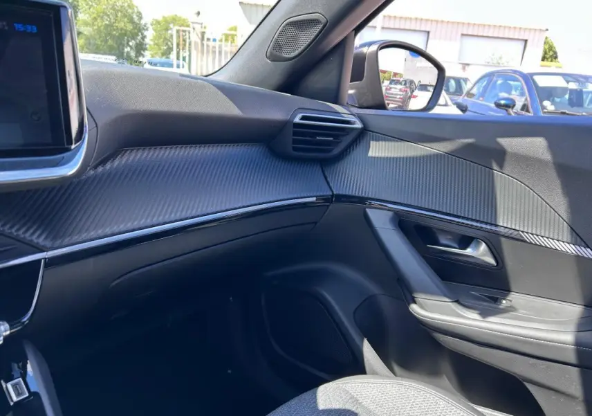 Vue intérieure côté passager du Peugeot 2008 Hybrid 136 Allure 2025 noir, avec tableau de bord et garnitures effet carbone.