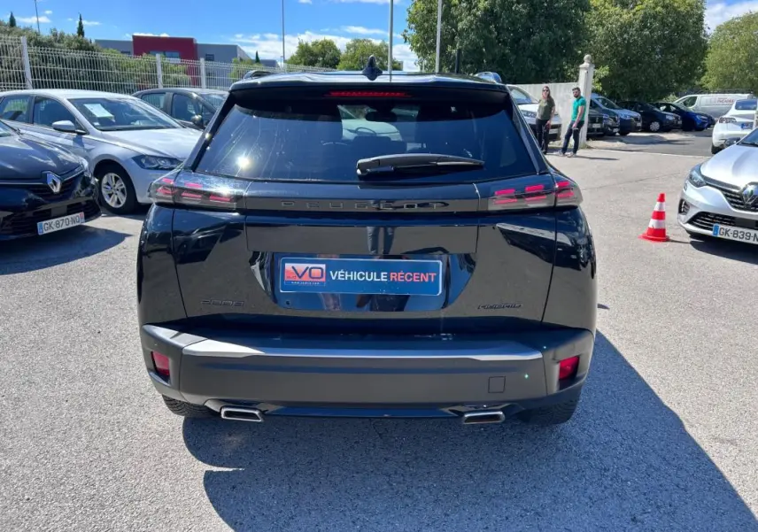 Vue arrière d’un Peugeot 2008 Hybrid noir 2025 avec barres de toit et double sortie d’échappement visible en extérieur.