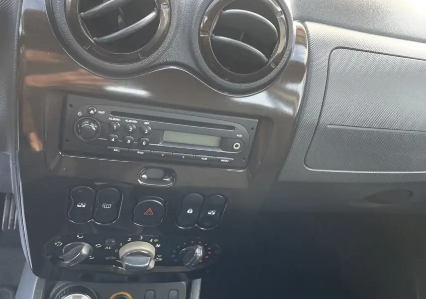 Vue rapprochée du tableau de bord gris foncé du Dacia Duster 2011, avec commandes climatisation et levier de vitesses manuel.