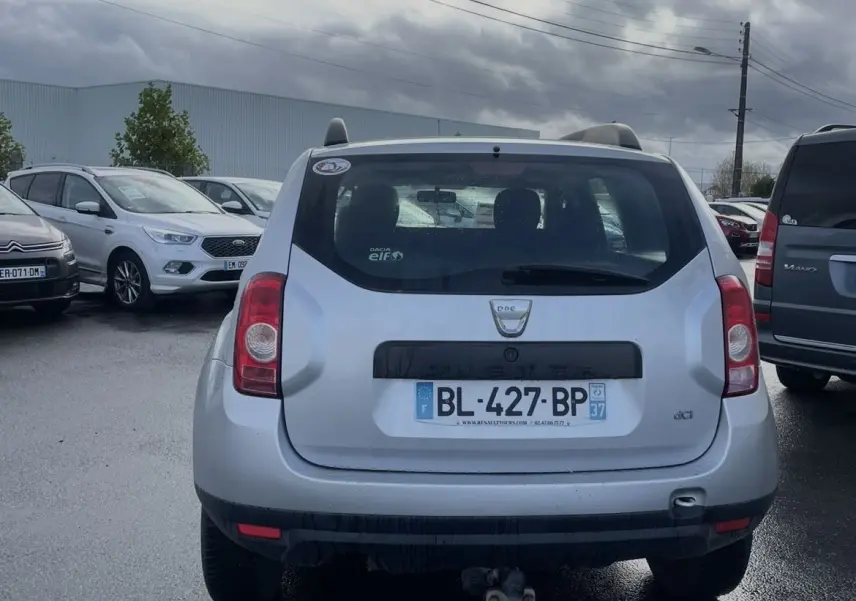 Vue arrière d'un Dacia Duster gris avec attelage et vitres teintées sous un ciel nuageux.