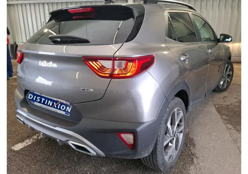 Vue 3/4 arrière droit d'un KIA STONIC gris météore 2024 avec feux allumés et finition GT Line visible en intérieur d'atelier.