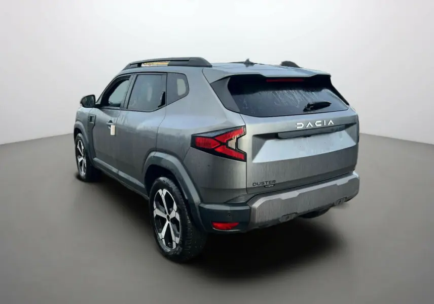 Vue 3/4 arrière droite d'un Dacia Duster noir nacré avec jantes alu 18 pouces et barres de toit visibles.