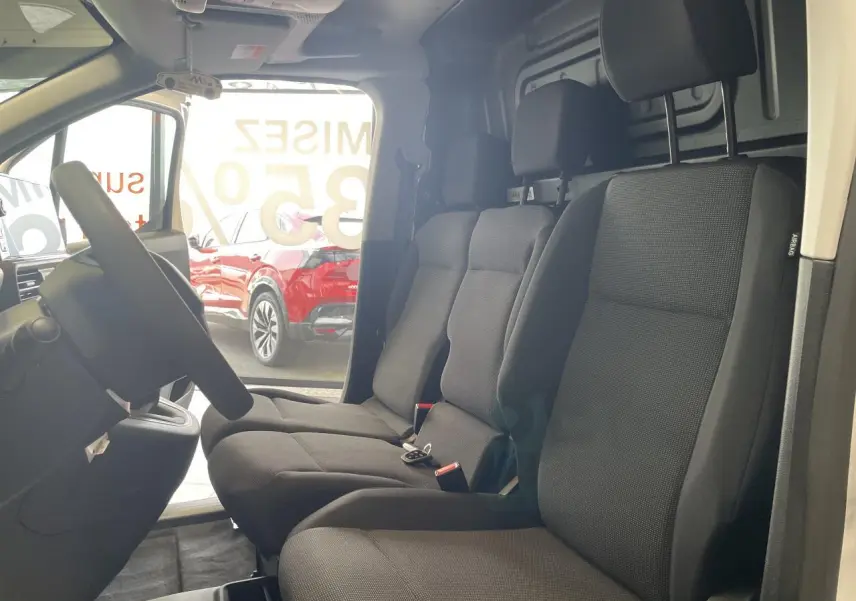 Vue intérieure côté conducteur du Peugeot Partner blanc, montrant la banquette passager 3 places en tissu noir.