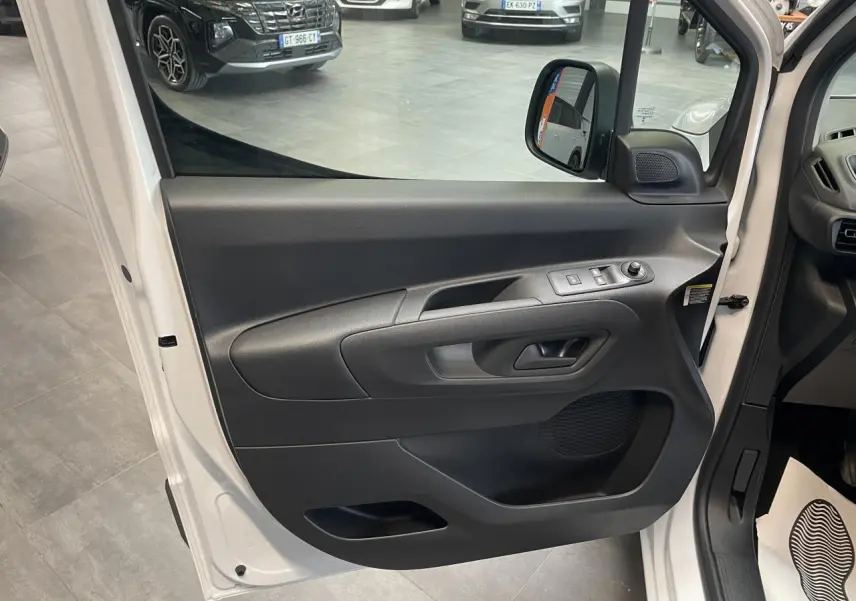 Vue rapprochée de la porte avant gauche blanche du Peugeot Partner 2026, avec commandes de vitres électriques et rétroviseur.