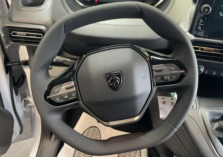Vue rapprochée du volant noir de la Peugeot Partner 2026 avec commandes intégrées et tableau de bord partiel visible.