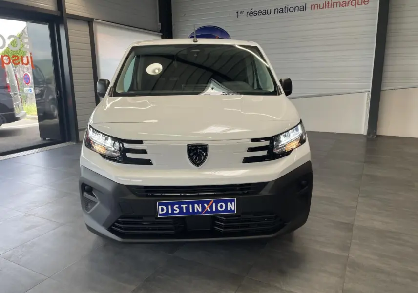 Vue avant d'un Peugeot Partner blanc 2026 avec calandre noire et logo lion au centre, en intérieur showroom.