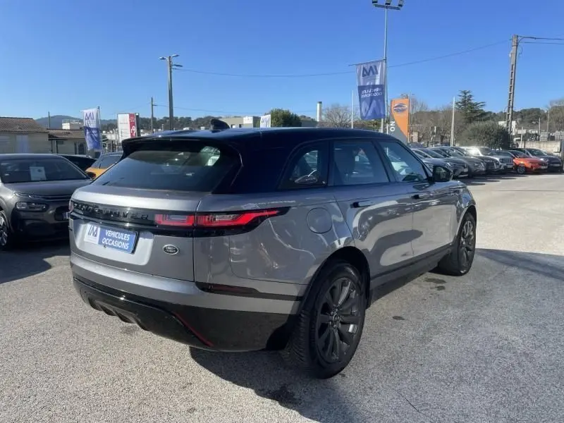 Vue 3/4 arrière droite d'un Range Rover Velar gris métal 2020 avec toit noir et jantes foncées sur parking.