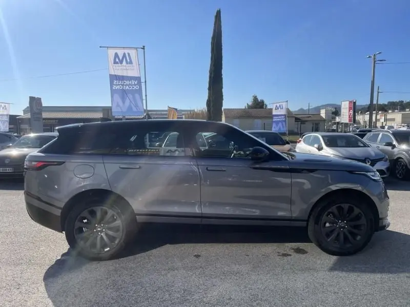 Profil côté gauche d'un Range Rover Velar gris métal 2020 avec jantes noires, garé en extérieur au soleil.