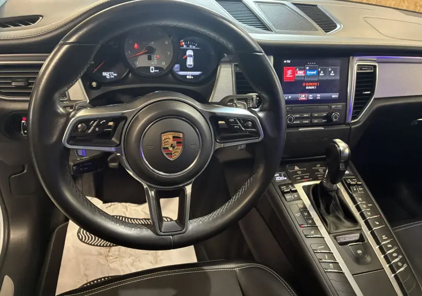 Vue intérieure du tableau de bord noir du Porsche Macan GTS 2017, avec volant cuir, écran tactile et levier de vitesses.