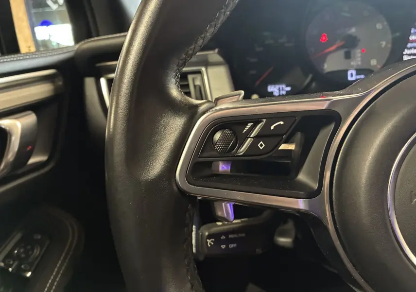 Gros plan sur la partie droite du volant cuir noir du Porsche Macan GTS 2017 avec commandes intégrées et tableau de bord flou.