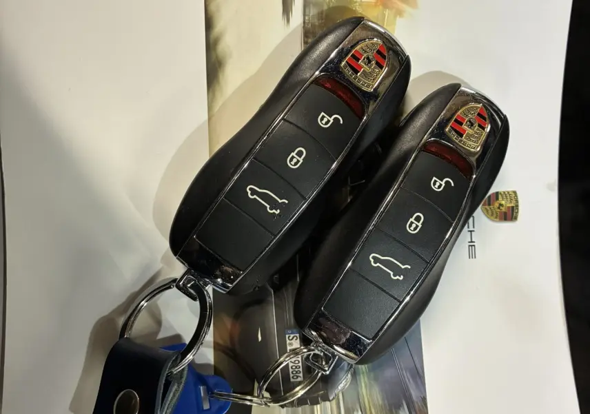 Gros plan sur deux clés noires Porsche Macan GTS posées sur une brochure avec logo et photo floue d'une voiture en mouvement.