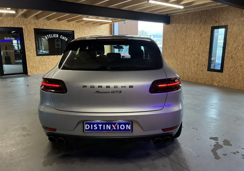 Vue arrière d'une Porsche Macan GTS grise stationnée en intérieur avec feux arrière allumés et double sortie d'échappement.