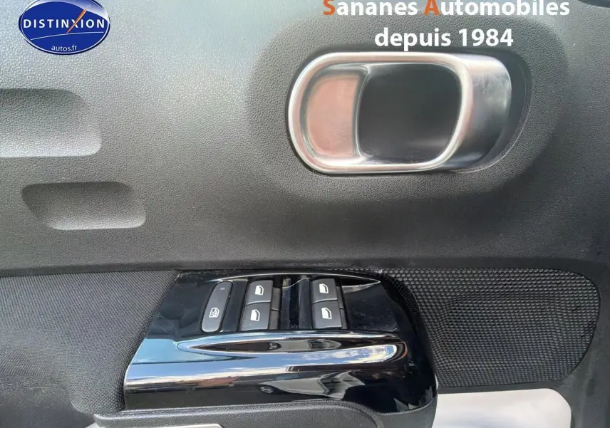 Gros plan sur la poignée intérieure et les commandes de lève-vitres côté gauche d’une Citroën C3 blanche.