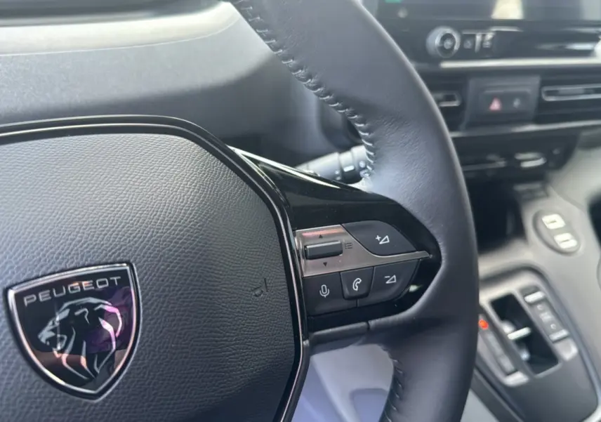 Gros plan sur le volant cuir multifonctions du Peugeot Rifter 2026 avec logo lion et commandes intégrées.