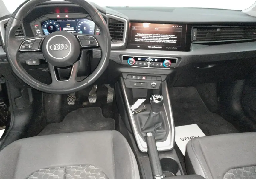 Vue intérieure avant de l'Audi A1 Sportback 2023 noire, avec volant multifonction, tableau de bord digital et levier de vitesse manuel.