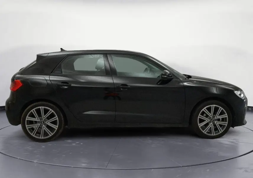 Profil droit d'une Audi A1 Sportback noire 2023 avec jantes alliage et lignes épurées, sur fond neutre intérieur.