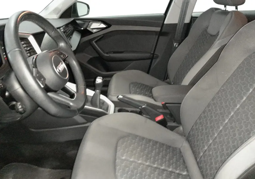 Vue intérieure côté conducteur de l’Audi A1 Sportback 2023, sièges sport gris avec volant cuir et levier de vitesse manuel.