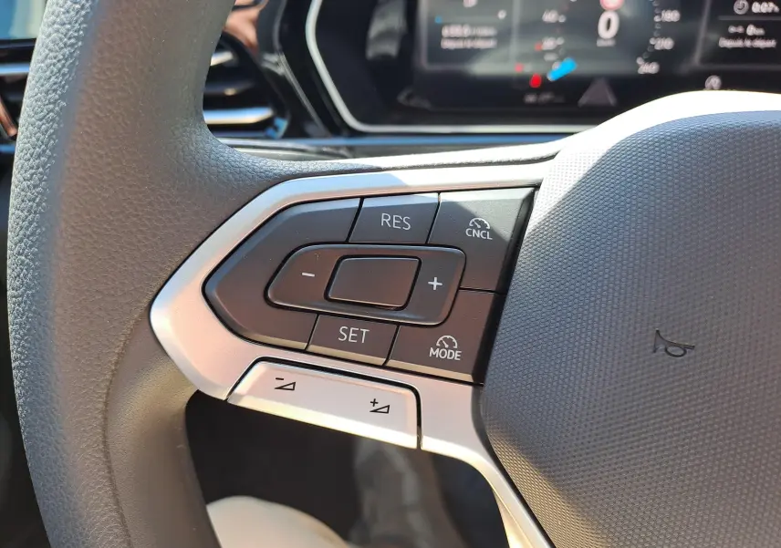 Gros plan sur les commandes au volant à gauche du Volkswagen Caddy Cargo Maxi blanc, avec régulateur de vitesse et affichage numérique en arrière-plan.