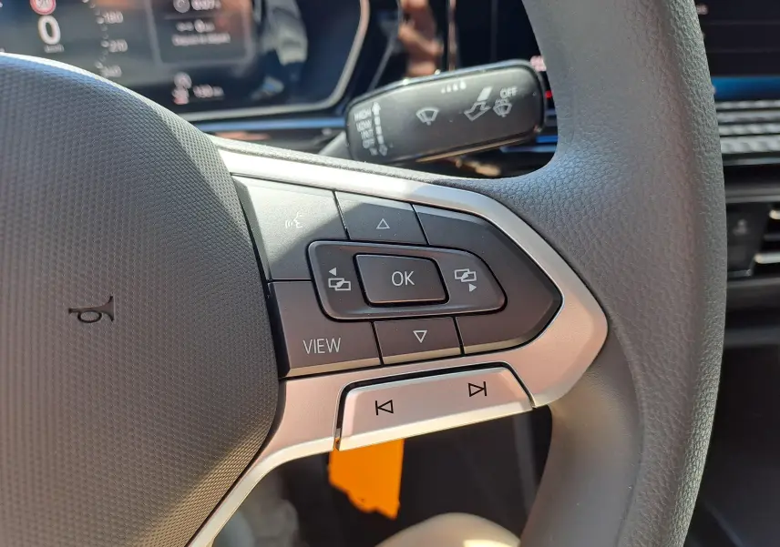 Gros plan sur les commandes multifonctions à droite du volant du Volkswagen Caddy Cargo Maxi blanc, tableau de bord en arrière-plan.
