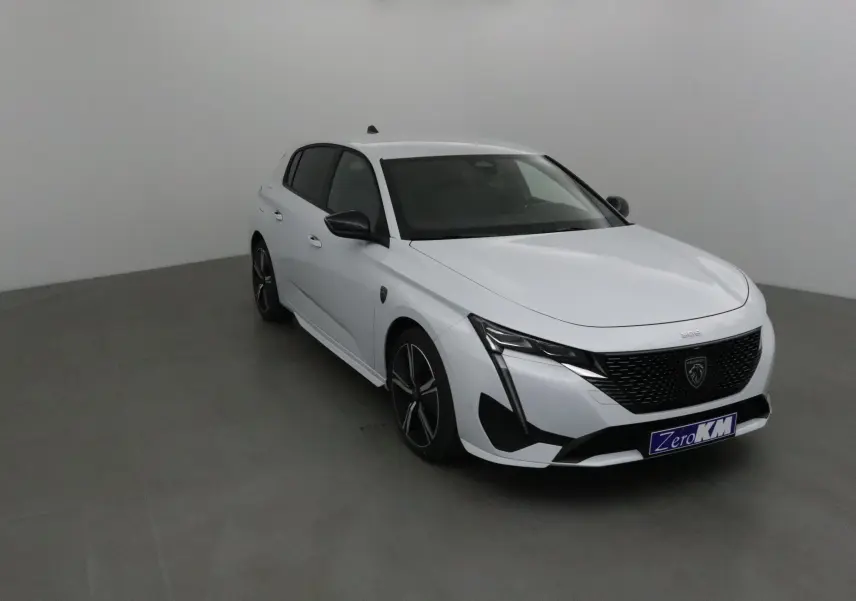 Peugeot 308 blanc Okenite vue 3/4 avant droit dans un intérieur neutre avec jantes noires distinctives.