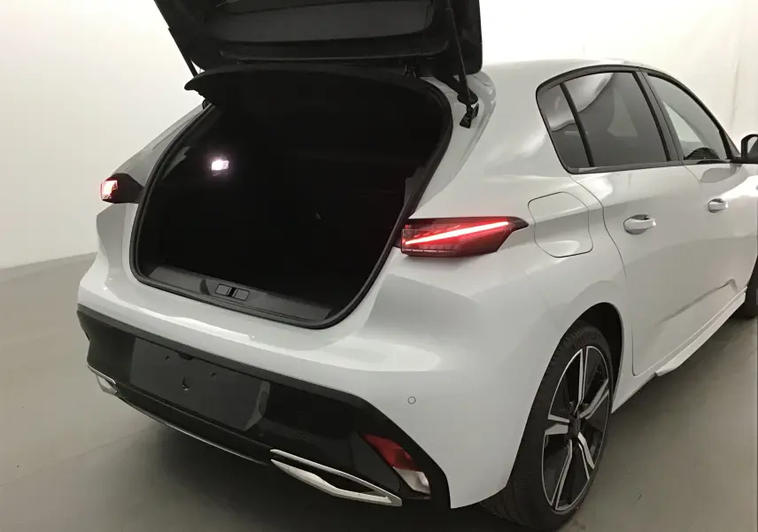 Vue 3/4 arrière droite d'une Peugeot 308 blanche Okenite avec coffre ouvert et feux arrière allumés.