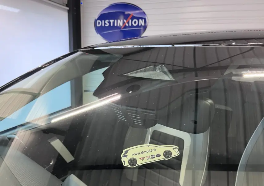 Gros plan sur le pare-brise avant d'une Citroën C4 noire métallisée avec un pendentif voiture suspendu à l'intérieur.