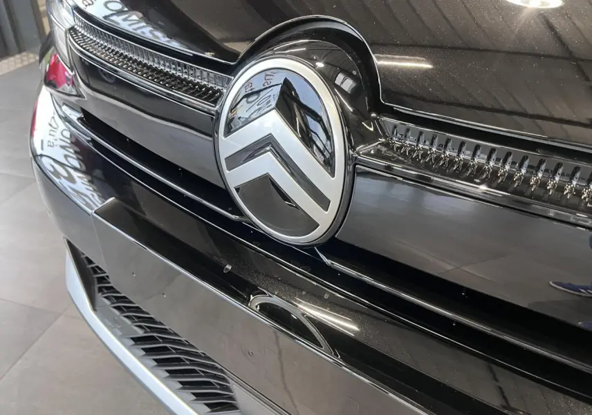 Gros plan sur la calandre avant noire métallisée d'une Citroën C4 2025 avec logo chrome distinctif au centre.