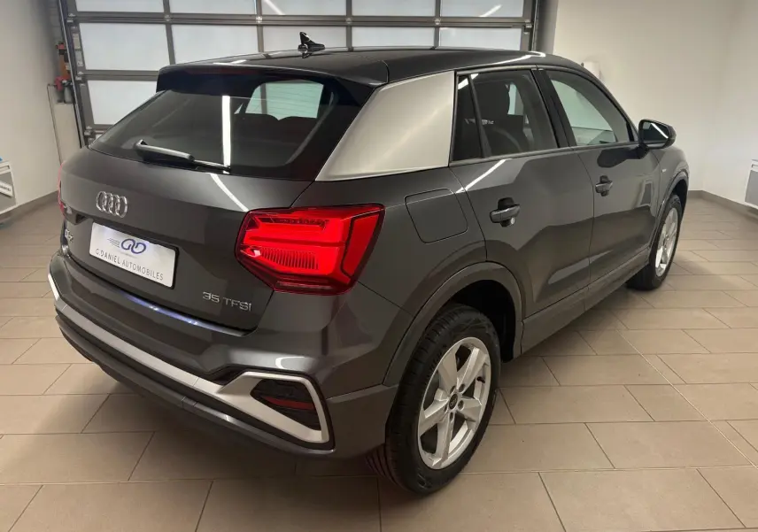 Audi Q2 35 TFSI S line gris Daytona en 3/4 arrière droit, avec hayon électrique et jantes alliage visibles.