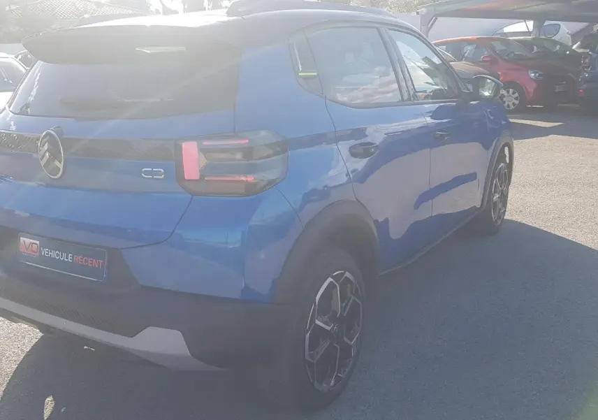 Vue 3/4 arrière droite d'une Citroën C3 bleu foncé 2024 avec jantes alliage 17 pouces et barres de toit.