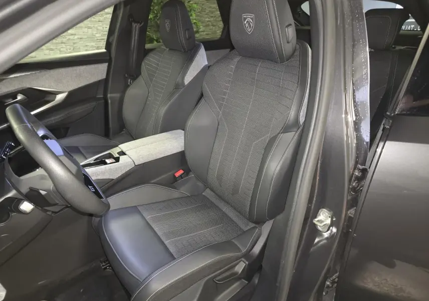 Vue intérieure côté conducteur du Peugeot 3008 gris 2025, sièges tissu et cuir avec logo Peugeot brodé sur les appuie-têtes.