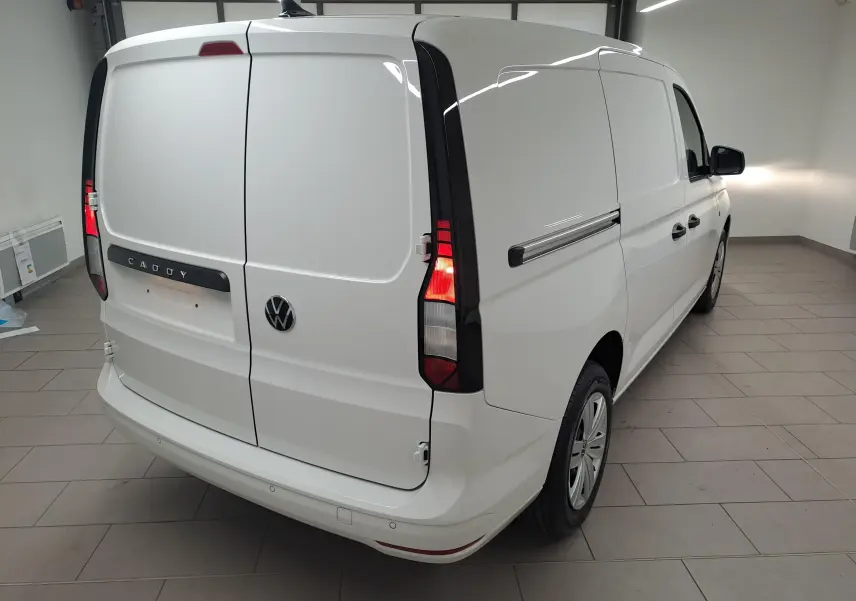 Vue 3/4 arrière droite du Volkswagen Caddy Cargo Maxi blanc Candy avec feux arrière allumés dans un intérieur.