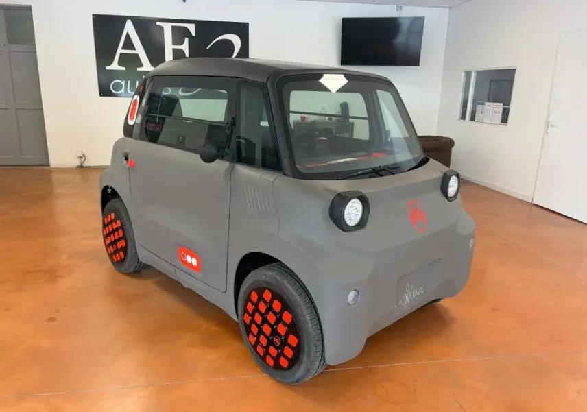 Vue 3/4 avant droite d'une Citroën AMI Spicy grise électrique 2025 avec jantes et logos orange distinctifs.
