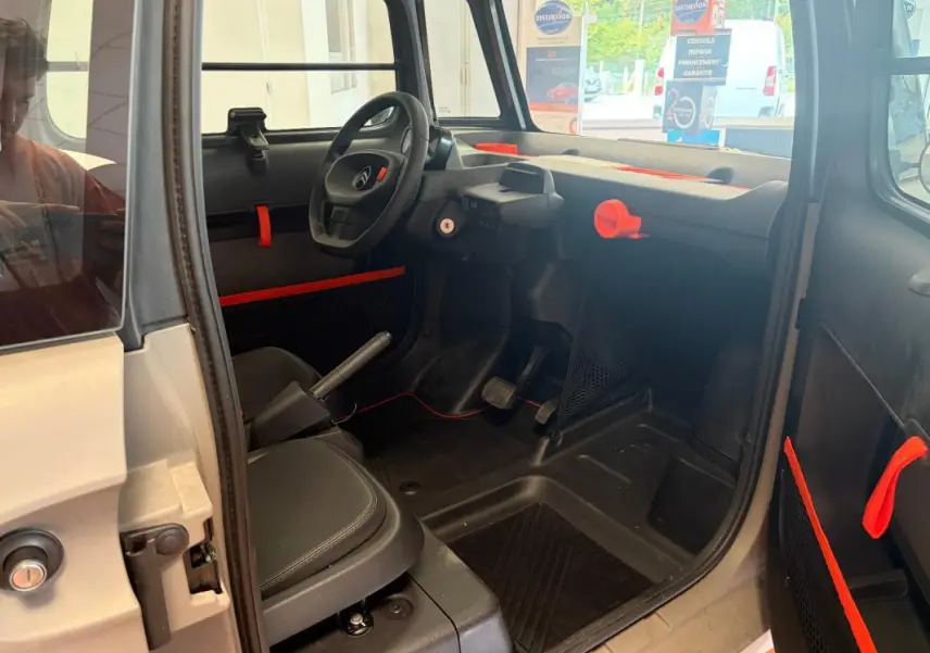 Intérieur de la Citroën AMI Spicy 2025 gris, vue côté conducteur, avec détails orange vif sur tableau de bord et portes.
