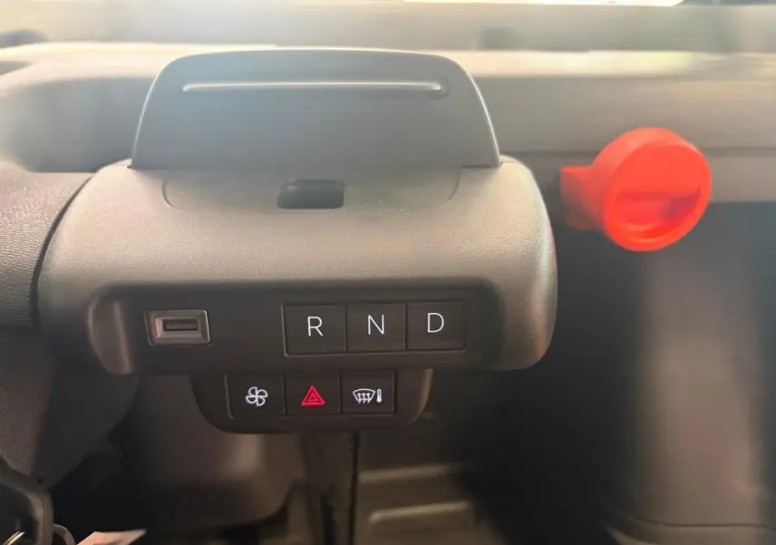 Gros plan sur la console centrale de la Citroën Ami Spicy 2025 grise, montrant les boutons de boîte auto R, N, D et un bouton rouge d'alerte.