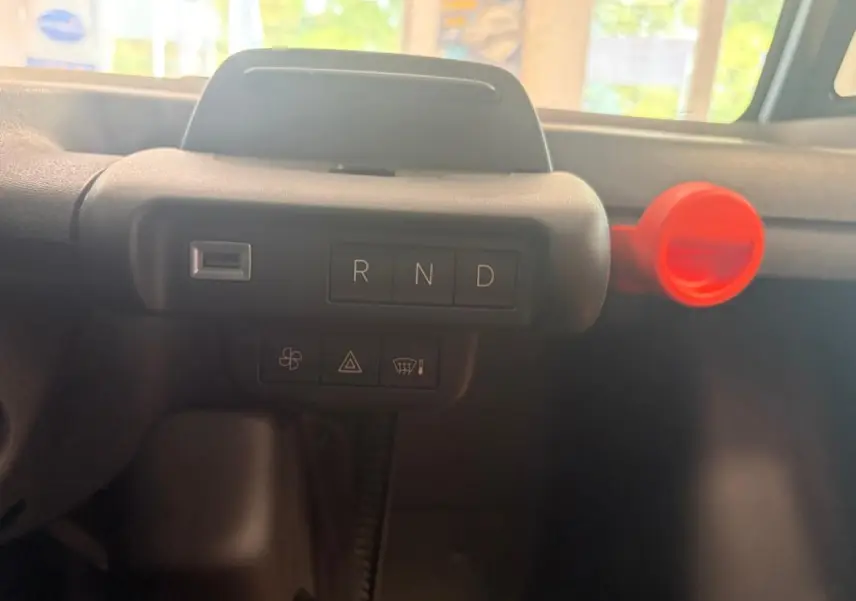 Détail du tableau de bord de la Citroën Ami Spicy 2025, montrant la commande de boîte auto gris foncé avec bouton rouge.