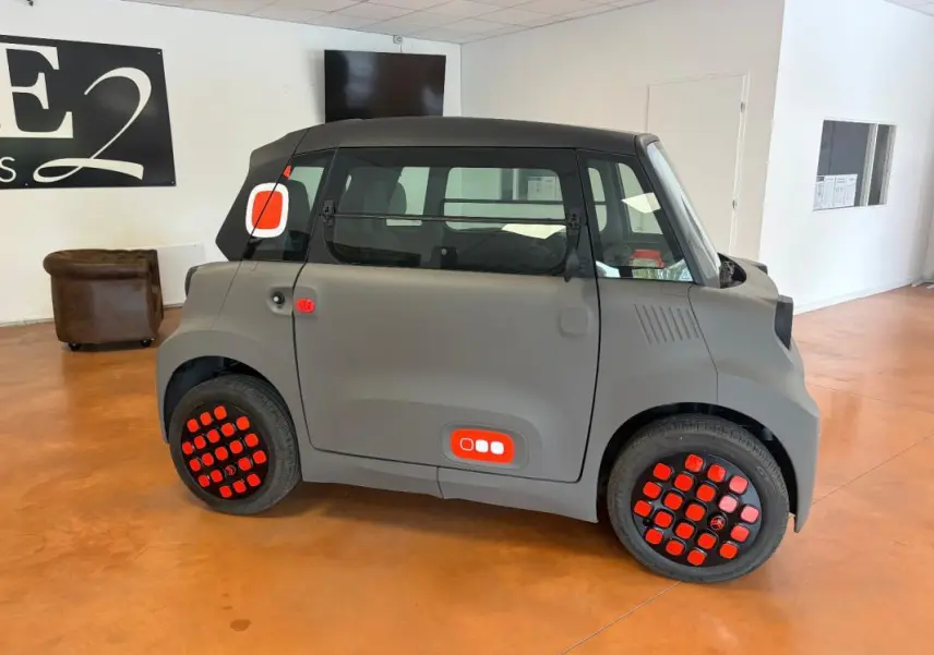 Vue de profil droit de la Citroën Ami Spicy gris 2025 avec détails rouges distinctifs sur les roues et la carrosserie.