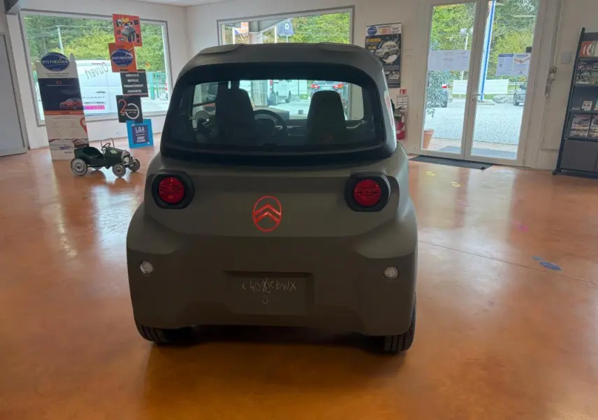 Vue arrière du Citroën Ami Spicy gris 2025, compacte et électrique, avec feux ronds rouges et logo Citroën éclairé.