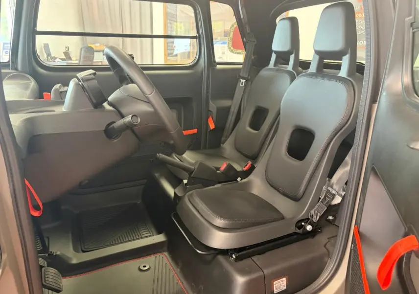 Vue intérieure côté gauche du Citroën Ami Spicy 2025 gris, montrant les sièges noirs et détails orange vifs.