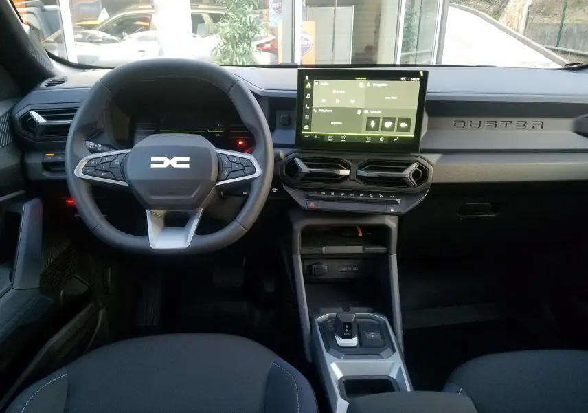 Vue intérieure frontale du tableau de bord du Dacia Duster 2025, avec volant multifonction et écran tactile central.