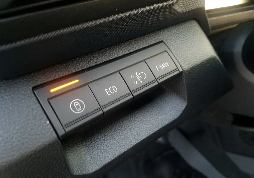 Gros plan sur les boutons de commande du tableau de bord du Dacia Duster gris schiste, avec témoin orange allumé.