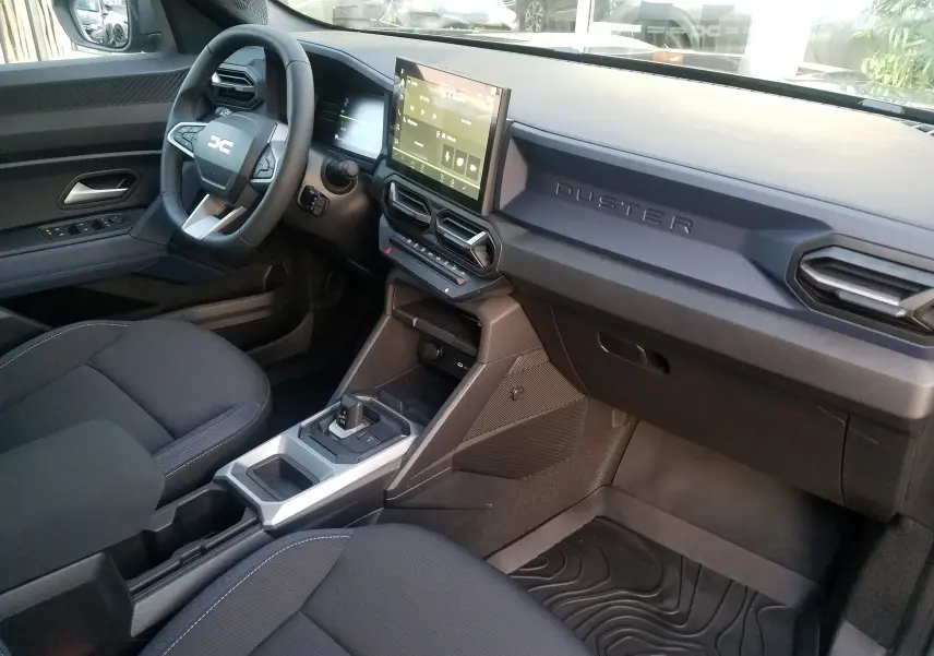 Intérieur du Dacia Duster 2025 vu côté conducteur, tableau de bord gris avec écran tactile et volant multifonction.