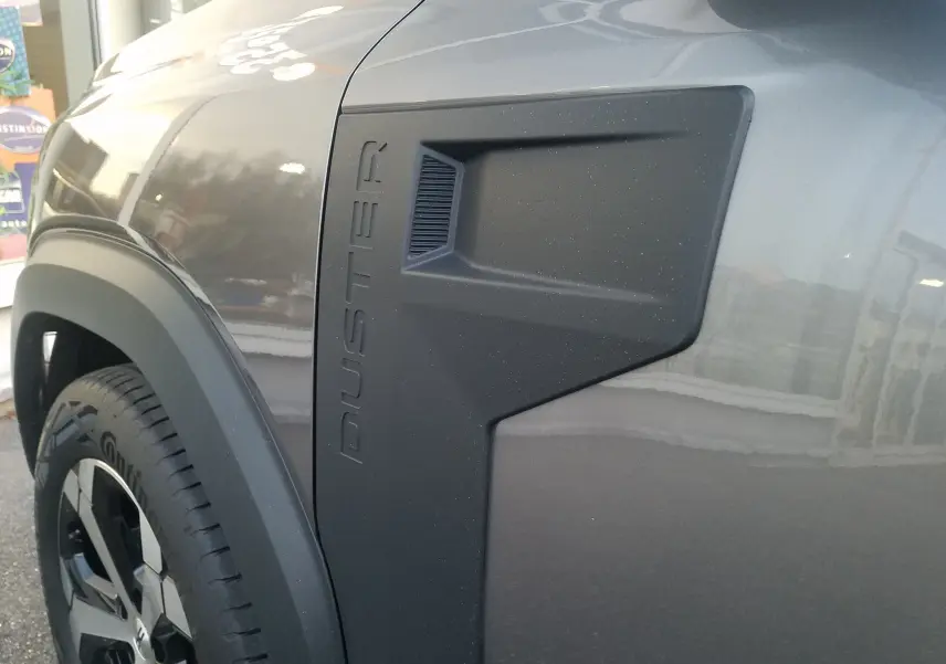 Gros plan sur l'aile avant gauche gris schiste du Dacia Duster 2025 avec logo PUSTER en relief noir mat.