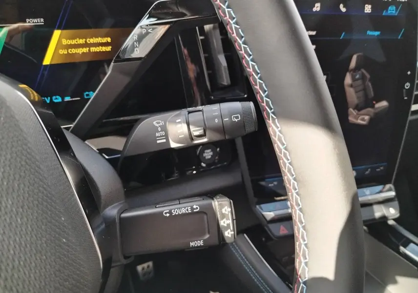 Gros plan sur le volant avec surpiqûres tricolores et commandes, tableau de bord numérique du Renault Austral E-Tech 2025.