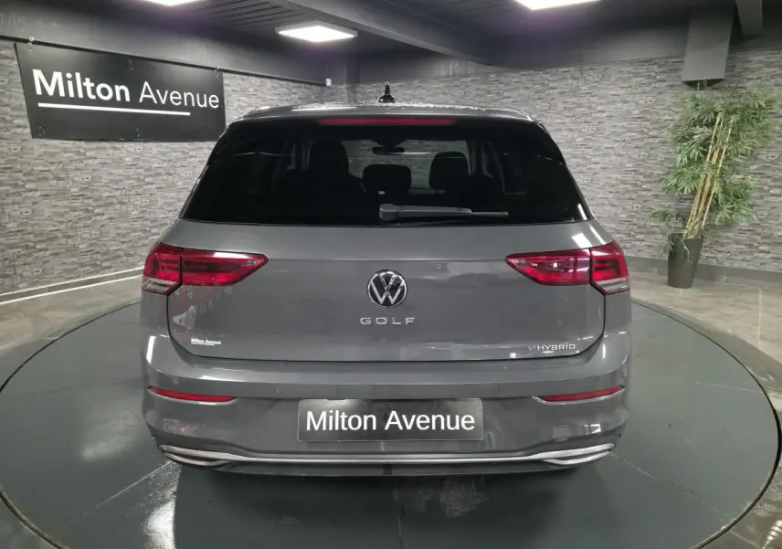 Vue arrière d'une Volkswagen Golf gris Urano hybride rechargeable, avec feux LED et lunette arrière surteintée en intérieur showroom.