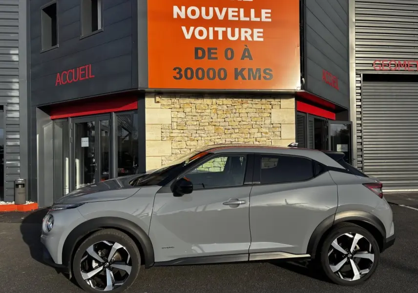 Profil droit d'un Nissan Juke Hybrid gris clair 2024 avec jantes noires et détails noirs contrastants.
