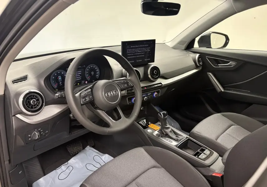 Vue intérieure côté conducteur de l'Audi Q2 35 TFSI 150 S tronic 7 S line avec tableau de bord moderne et écran central.