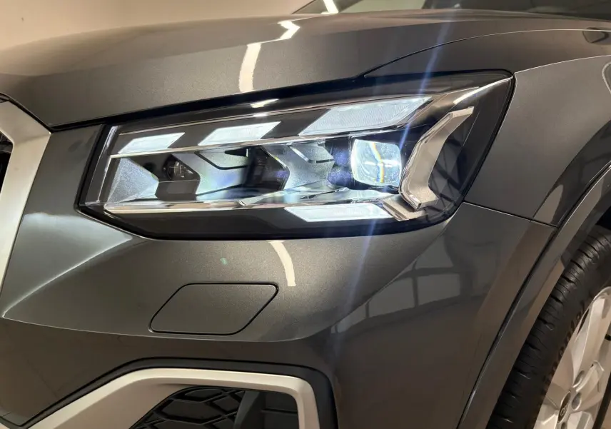 Gros plan sur le phare avant droit de l'Audi Q2 35 TFSI S Line en gris Daytona métallisé.